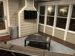 A room with a TV mounted on a wall, a trash can, a black table, and a gray and white patterned rug.