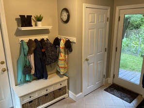 A hallway with a coat rack, a clock, a door, and a bench with baskets.
