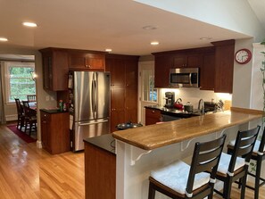 A kitchen with wooden cabinets, a stainless steel refrigerator, a microwave, and a wooden island with bar stools.