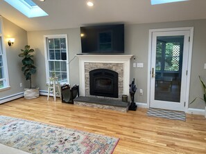 A living room with a fireplace, a television mounted above it, and a large window.