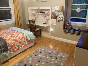 A bedroom with a bed, a desk, a chair, a rug, and a window.