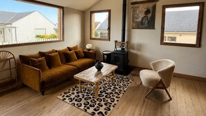 Ein Wohnzimmer mit einer Couch, einem Couchtisch, einem Sessel, einem Kamin und großen Fenstern.