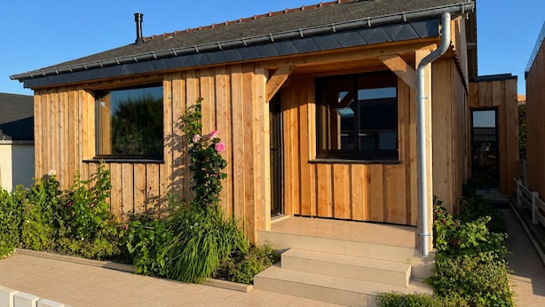 Ein Holzhaus mit zwei Fenstern, einem Schornstein und einer kleinen Veranda mit Stufen.