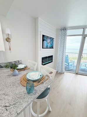 Eine moderne Küche mit Fernseher, Esstisch und Meerblick vom Balkon aus.