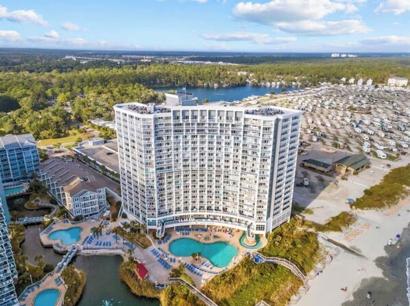 Ein Hochhaus-Hotel mit mehreren Balkonen, einem Pool und einem Strandbereich.