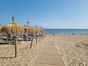 A beach with sun loungers and thatched umbrellas, a wooden walkway, and the ocean. - Coronado Beach (Marbella)