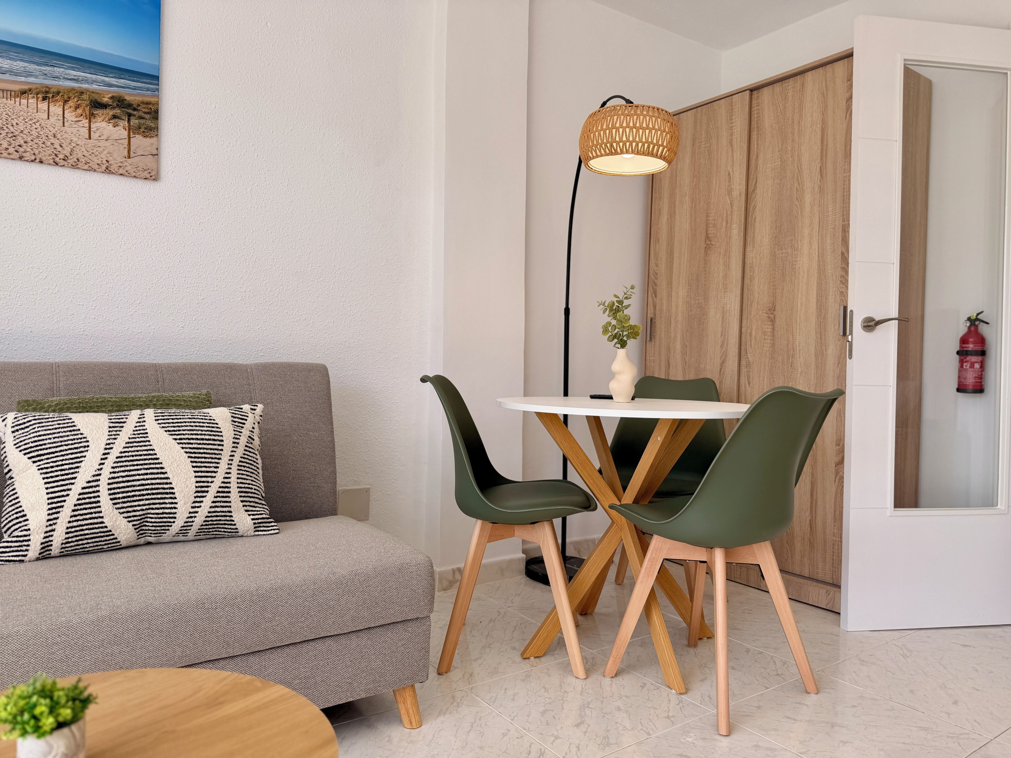 Una sala de estar moderna con un sofá, una mesa de comedor con sillas, una lámpara de pie y una puerta de madera.