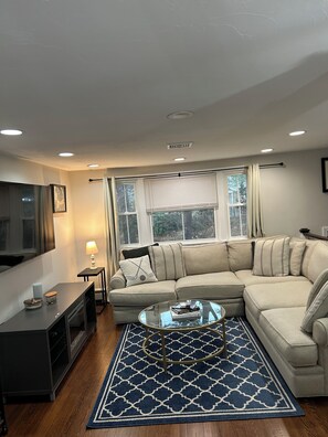 A living room with a sectional sofa, a glass coffee table, a TV, a lamp, and a patterned rug. - World Cup Ready Home, 10 minutes to Stadium! (Foxborough)