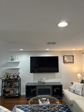 A living room with a flat-screen TV, a glass coffee table, a sofa, a TV stand, and a bar cart with bottles. - World Cup Ready Home, 10 minutes to Stadium! (Foxborough)