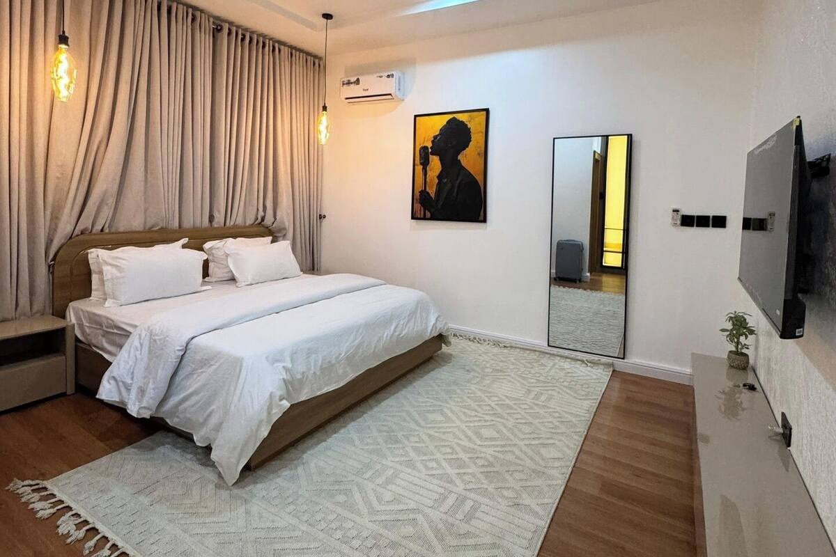 A bedroom with a bed, a large mirror, a TV, and an air conditioning unit.