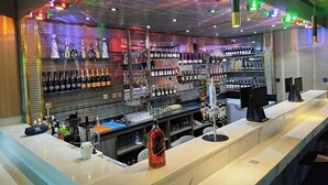 A bar area with shelves of bottles, a counter with a beverage dispenser, and a ceiling with colorful lights. - Dorville Hotel And Suites (Orerokpe)
