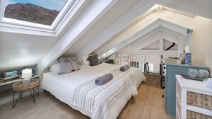 Ein Schlafzimmer mit hohen Decken und einem Oberlicht, ein Bett mit Kissen, ein Nachttisch und ein kleiner Stuhl.