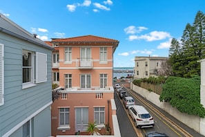 A multi-story building with a red-tiled roof, a balcony, and a view of the sea.