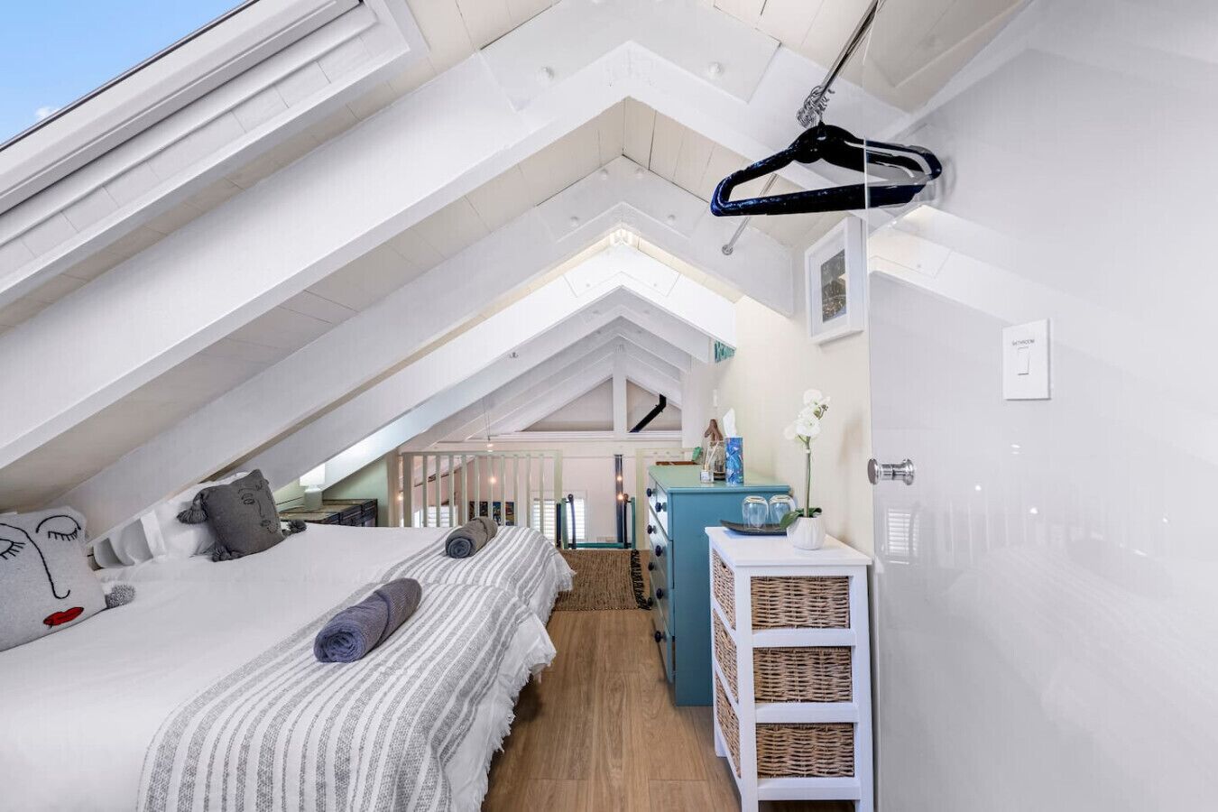 A high-ceilinged attic bedroom with a sloped roof, a bed with a striped blanket, a dresser, and a hanging coat rack.