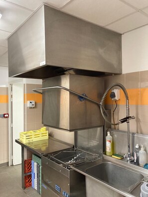 Eine gewerbliche Küche mit Edelstahlgeräten, einer Spüle und Lagerboxen.