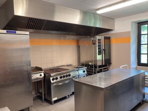Eine gewerbliche Küche mit Edelstahlgeräten, einem großen Ofen und einer Ablufthaube.