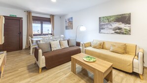 A living room with two sofas, a wooden coffee table, a dining table with chairs, a lamp, and a painting on the wall.