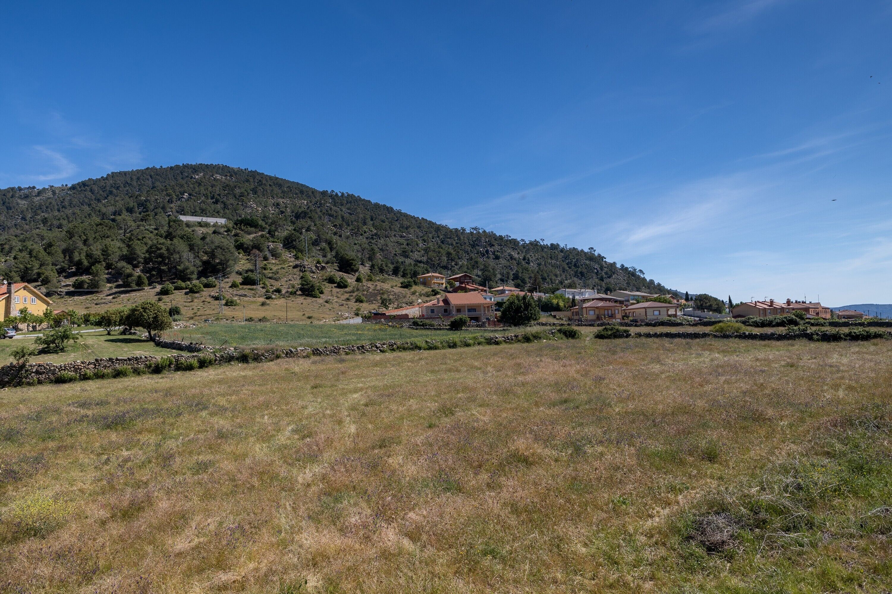 A rural landscape with houses on a hillside, stone walls, and a clear sky.