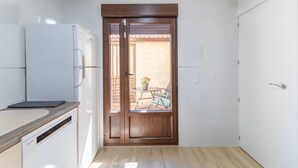 A compact kitchen with a dishwasher, a refrigerator, and a sliding door leading to an outdoor seating area.