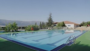 A swimming pool with a view of mountains, a fenced area, and a building with a red roof.