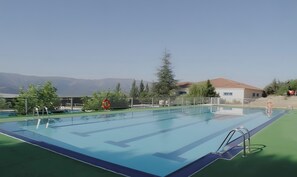 A swimming pool with a view of mountains, a fenced area, and a building with a red roof. - Chalet Pinara with Fireplace and Mountain Views in the Sierra de Gredos (El Barraco)