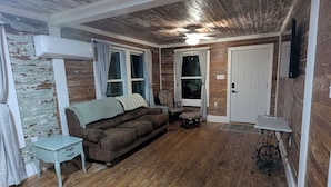 Una habitación con piso de madera, un sofá marrón, una mesita y un ventilador de techo.