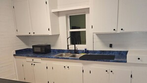 Una cocina con armarios blancos, encimera azul, microondas, fregadero y ventana.