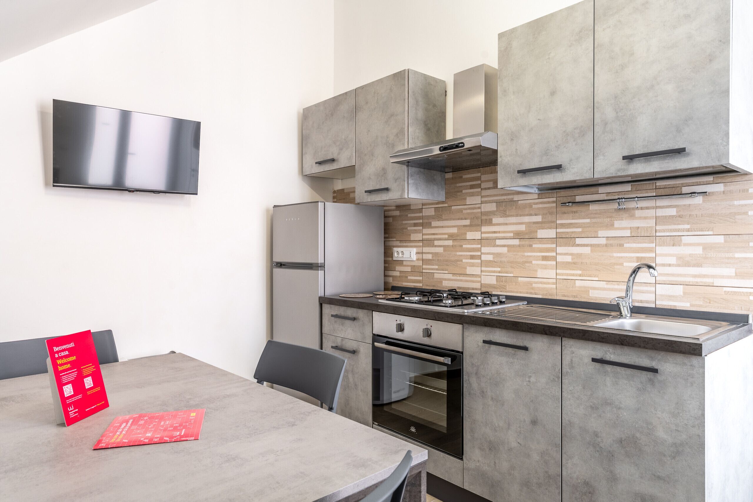 A modern kitchen with a built-in oven, a stainless steel sink, and a flat-screen TV mounted on the wall.