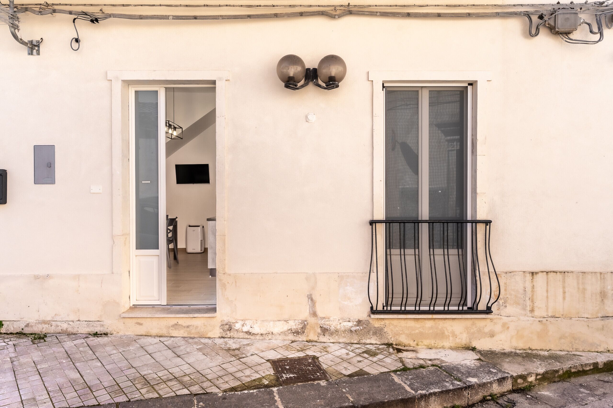 Un bâtiment dot é d’un porche carrelé, d’un balcon avec une rambarde en métal et d’une porte donnant sur un espace intérieur.