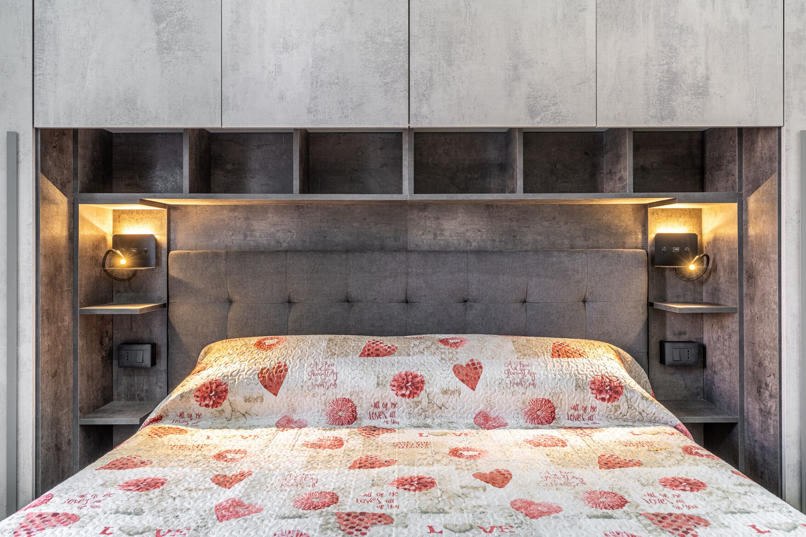 Una cama con colcha floral, cabecera con iluminación integrada y diseño moderno y minimalista.