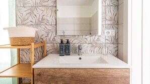 A bathroom with a white sink, wooden vanity, a mirror, and a wall with leaf-patterned tiles. - La Capinera by Wonderful Italy (Noto)