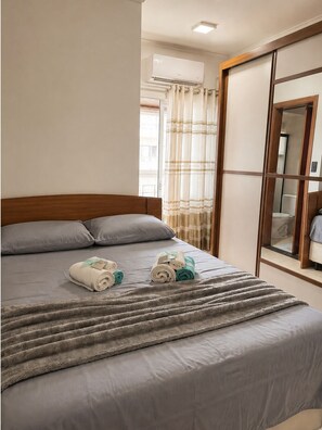 Quarto de hotel com cama, janela com cortinas, ar condicionado e guarda-roupa de madeira.