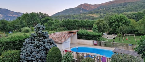 A residential area with a swimming pool, a fenced yard, and a view of mountains.