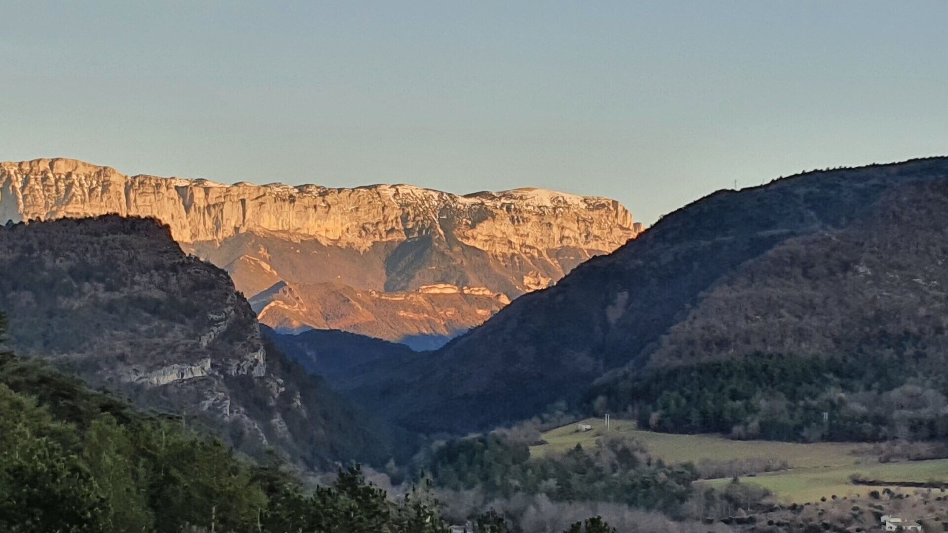 A mountainous landscape with a valley and a distant cliff.