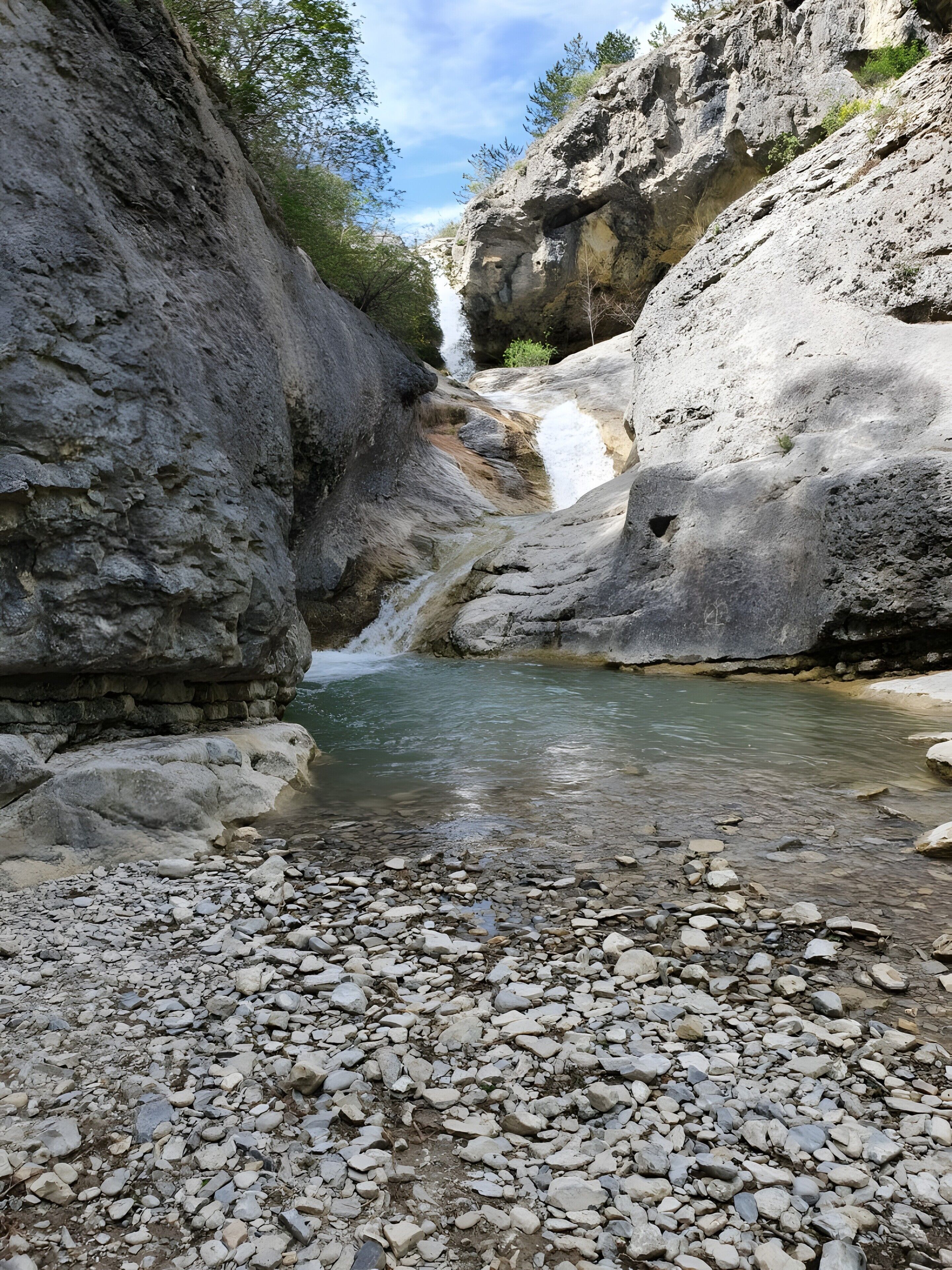 A rocky landscape with a clear stream, surrounded by cliffs and sparse vegetation.