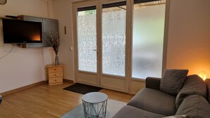 Un salón con un sofá, un televisor, un jarrón decorativo, una puerta corrediza de vidrio con vidrio esmerilado y una pequeña mesa redonda.