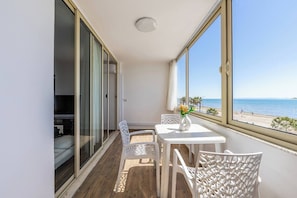 Ein Balkon mit Meerblick, ein weißer Tisch mit Stühlen und eine Vase mit Blumen.