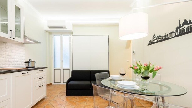 Uma cozinha moderna com armários brancos, um sofá preto, uma mesa de jantar de vidro e um mural com vista para a cidade.