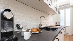 Cozinha moderna com máquina de café expresso embutida, pia e espaço para café da manhã, incluindo croissants e xícaras de café.