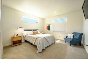 Une chambre à coucher comprenant un lit, une table de chevet, une chaise, une fenêtre et un téléviseur fixé au mur.