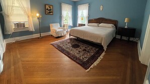 Una camera da letto con un letto, una sedia, un comodino, una lampada e una finestra con tende.