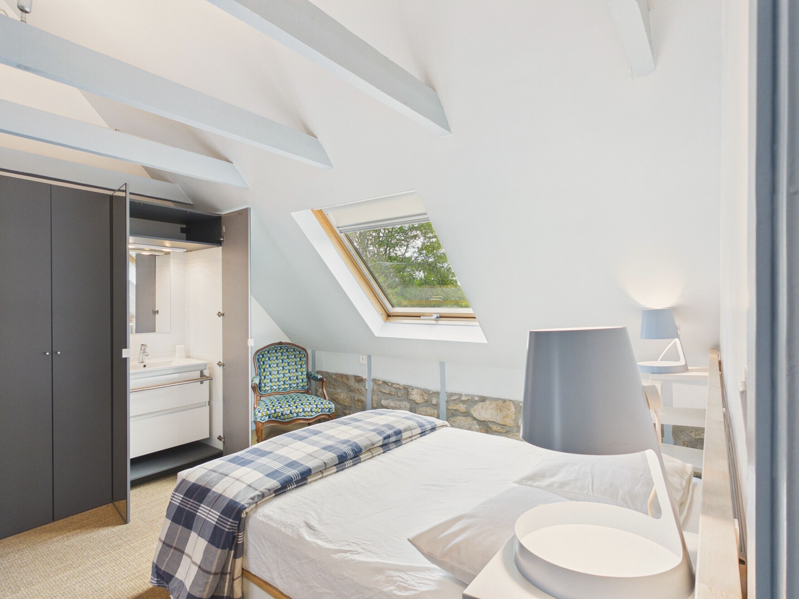 A bedroom with a skylight, a bed, a chair, a desk, and a wardrobe.