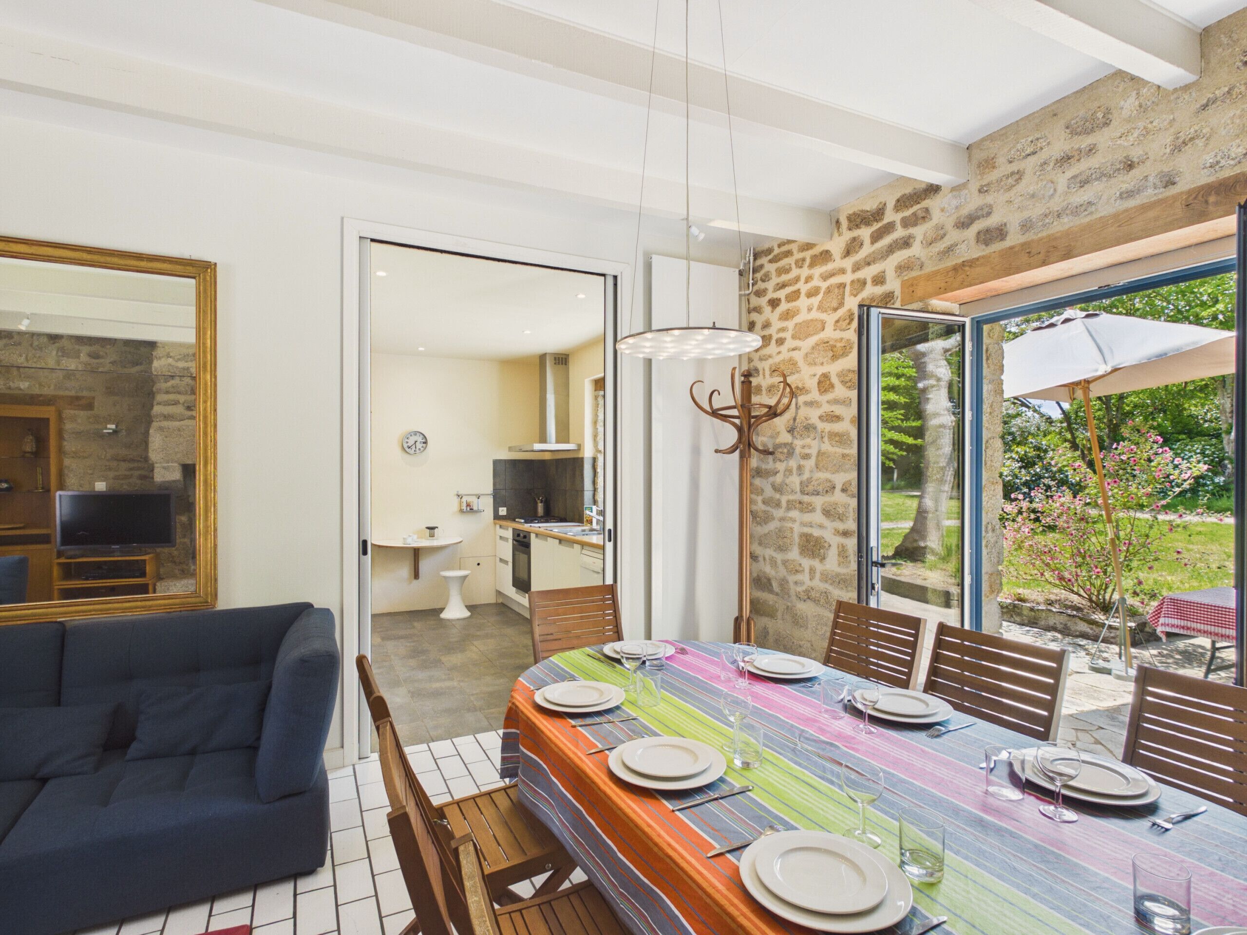 A dining area with a long table set for six, a sofa, and a stone wall.
