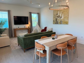 A modern living room with a sofa, TV, dining table, chairs, and a painting. - Turtle Nest Paradise - Quick Walk to Sand (Fort Myers Beach)