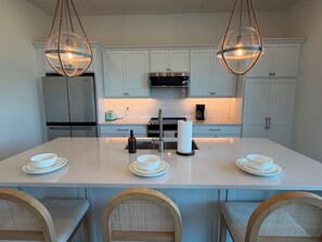 A modern kitchen with white cabinets, a central island with seating, and two pendant lights. - Turtle Nest Paradise - Quick Walk to Sand (Fort Myers Beach)