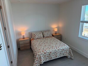 A bedroom with a bed, two bedside tables, and a window. - Turtle Nest Paradise (Fort Myers Beach)