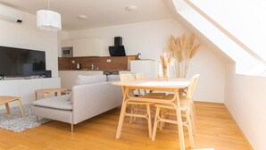 Ett modernt vardagsrum med en soffa, ett matbord med stolar, en platt-TV och ett kök i bakgrunden.