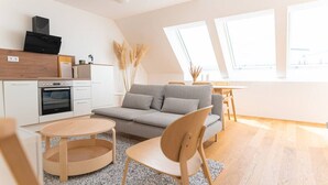 En modern lägenhet med kök, en grå soffa, ett matbord i trä och stora fönster.