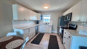 A compact kitchen with white cabinets, a microwave, a stove, and a sink. There is a window providing natural light. - Chill Vibes A - 2 min to Beach (Fort Myers Beach)