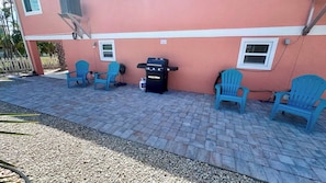 A patio with a grill, chairs, and a building with a pink facade. - Chill Vibes A - 2 min to Beach (Fort Myers Beach)